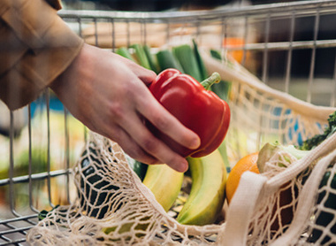 Person putting red pepper in basket at supermarket