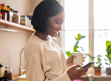 Woman in kitchen looking at phone with big smile on their face