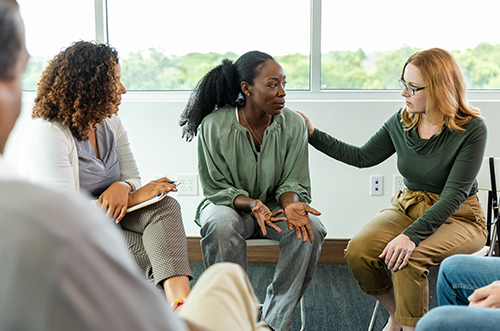 Image of a support group with a woman comforting and supporting another woman sat next to her