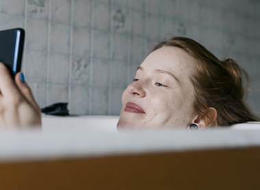 Woman in bath on phone looking happy