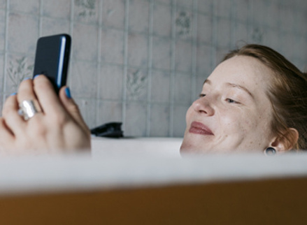 Woman in bath on phone looking happy