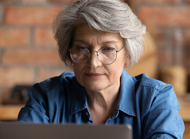 Elderly lady with glasses looking at laptop screen 