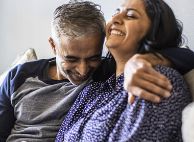 Couple hugging on sofa with smiles on their faces