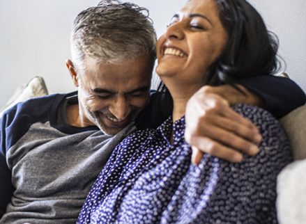 Couple hugging on sofa with smiles on their faces