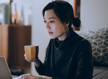 Woman with cup in hand looking at laptop