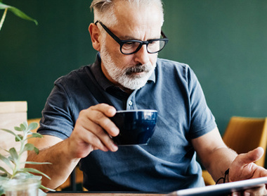 Man with cup of coffee in one hand and a tablet device in the other
