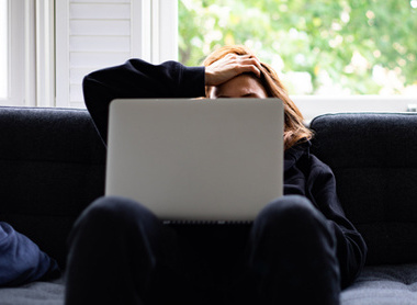 Woman on sofa, visible stressed in front of laptop